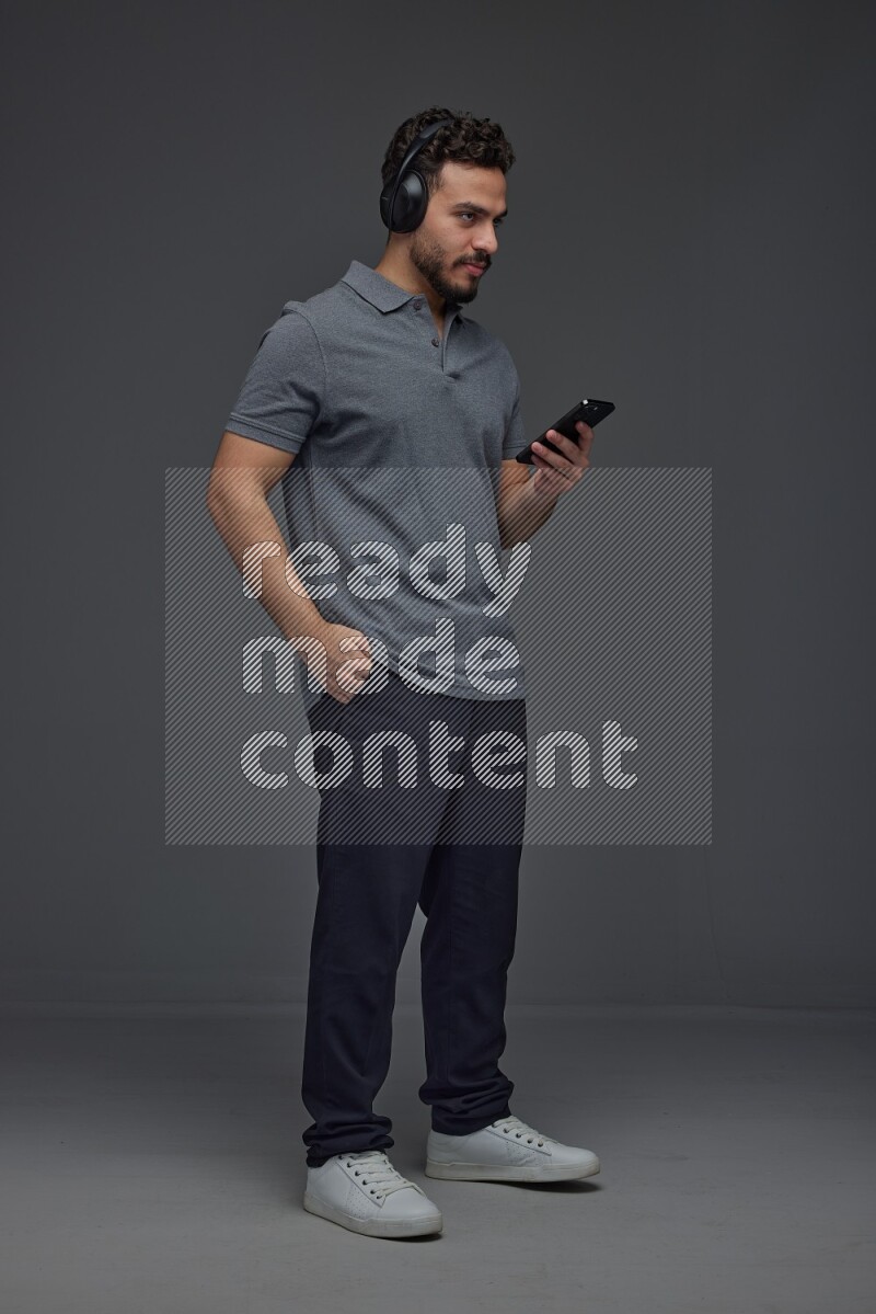 A man wearing casual and using his phone and headphone eye level on a gray background