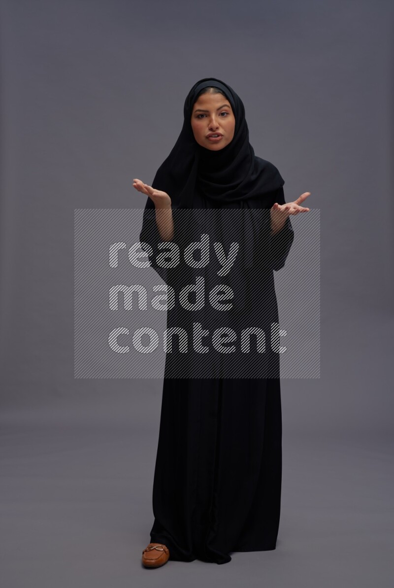 Saudi woman wearing Abaya standing interacting with the camera on gray background