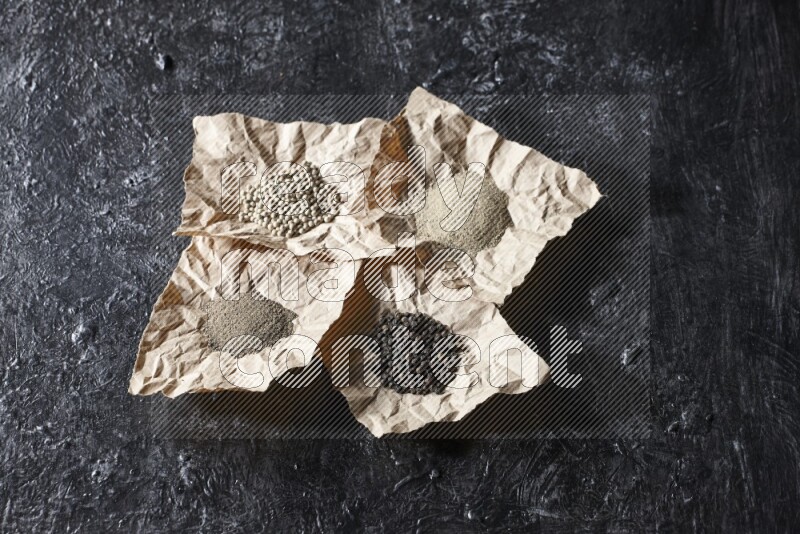 Crumpled pieces of paper full of black and white pepper beads and powder on a textured black flooring