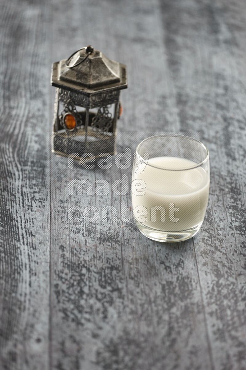 A silver lantern with different drinks, dates, nuts, prayer beads and quran on grey wooden background
