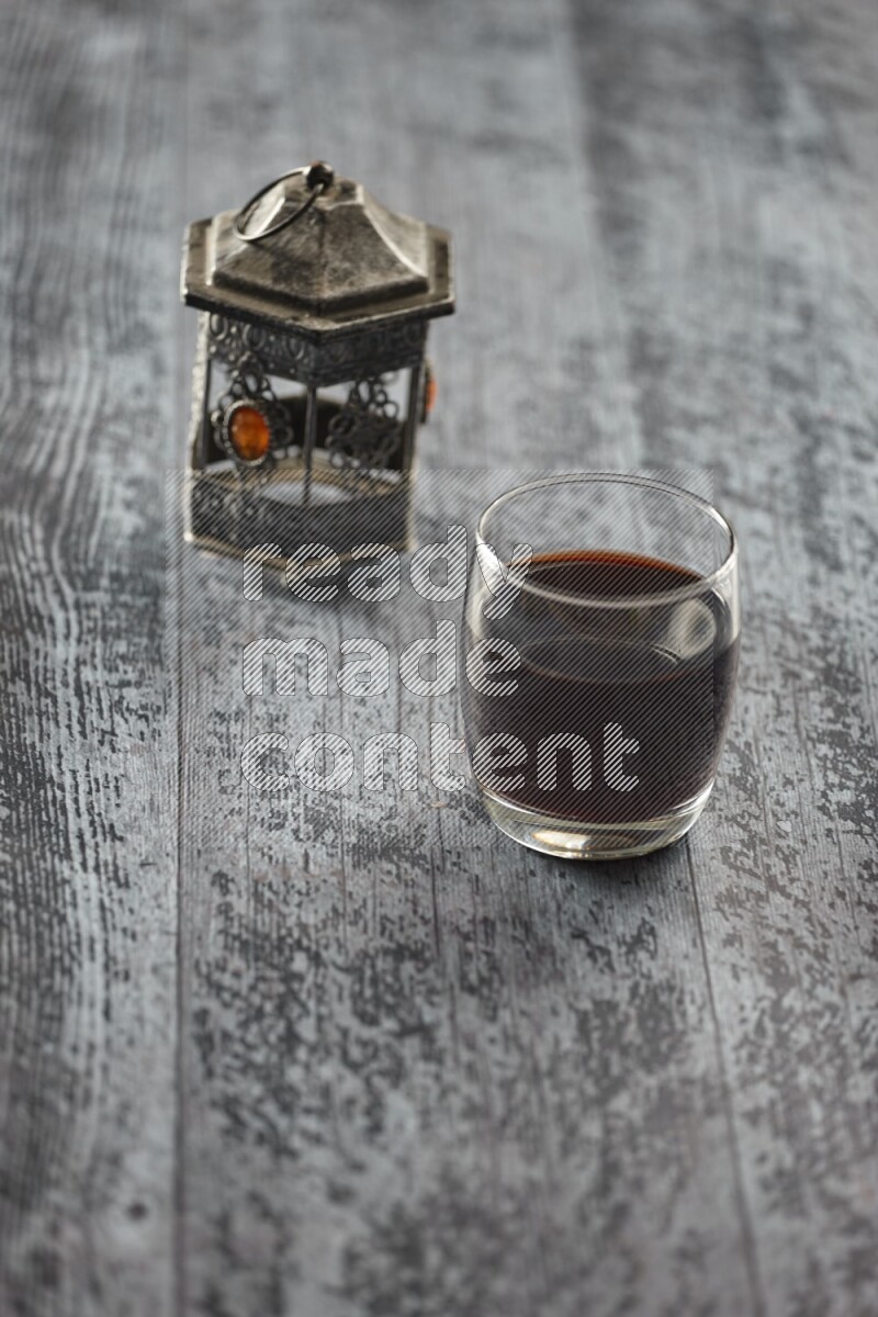 A silver lantern with different drinks, dates, nuts, prayer beads and quran on grey wooden background