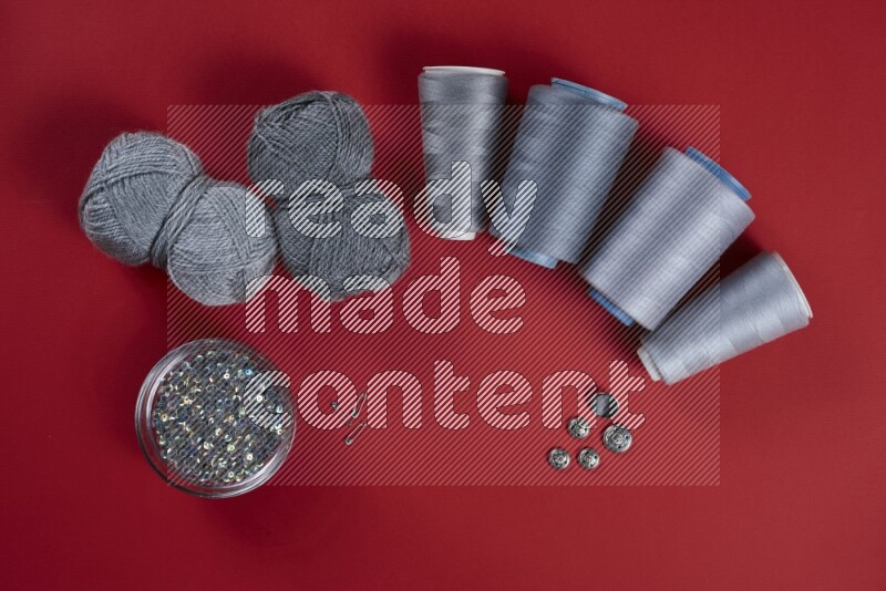 A grey collection of sewing and tailoring tools arranged on a red background