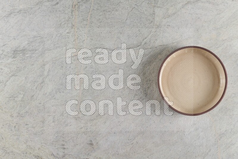A beige pottery oven bowl on grey marble background