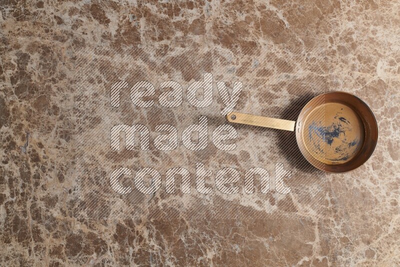 A small copper pan on beige marble background