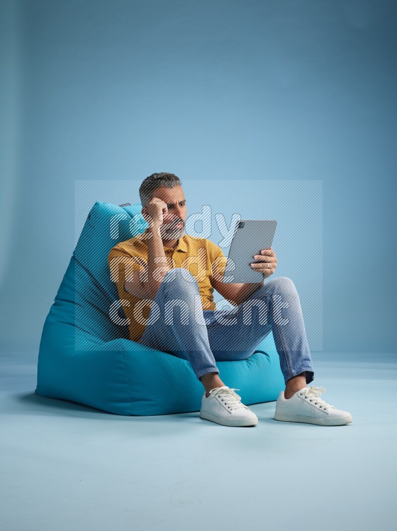 A man sitting on a blue beanbag and working on tablet
