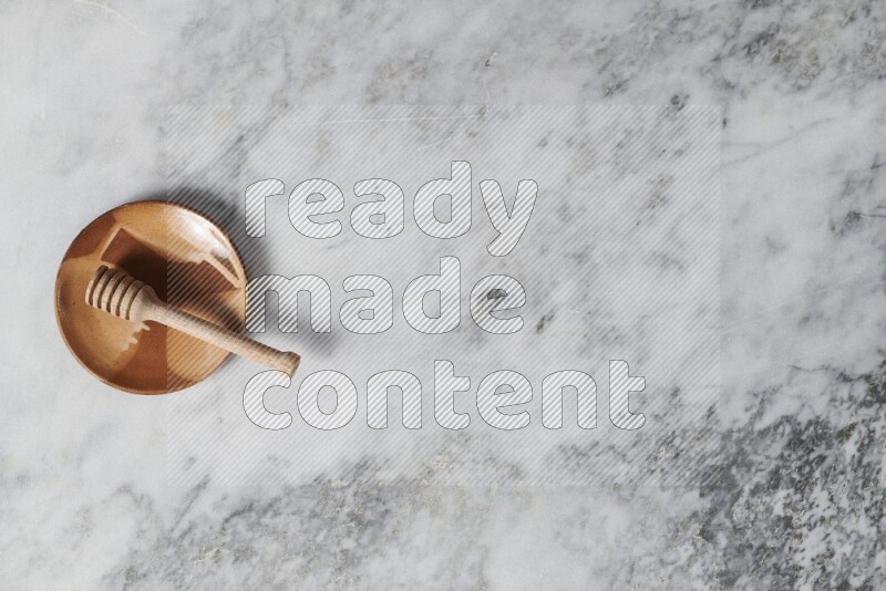 طبق فخاري متعدد الألوان مع ملعقة عسل خشبية بداخله على خلفية من الرخام الرمادي