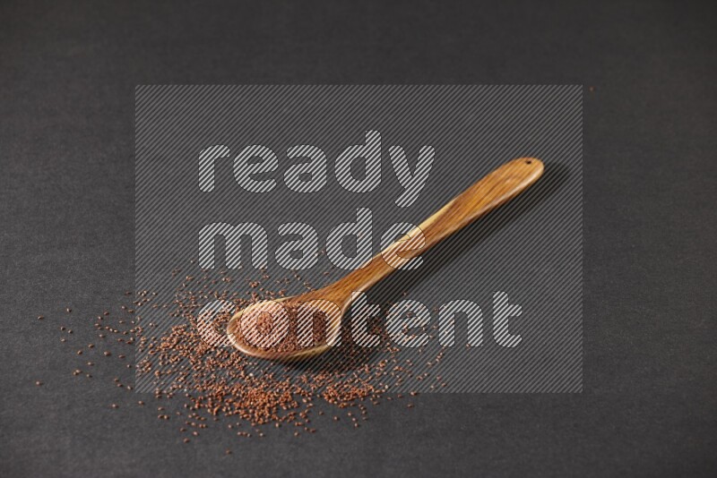 A wooden ladle full of garden cress seeds and seeds spread beside it on a black flooring