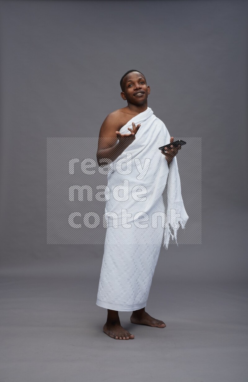 A man wearing Ehram Standing texting on phone on gray background