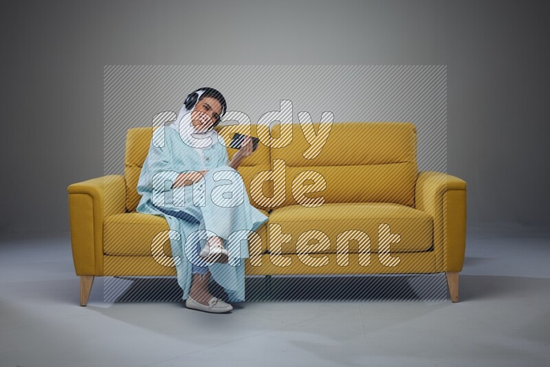 A Saudi woman sitting on a yellow Sofa Watching a Movie wearing Blue Abaya