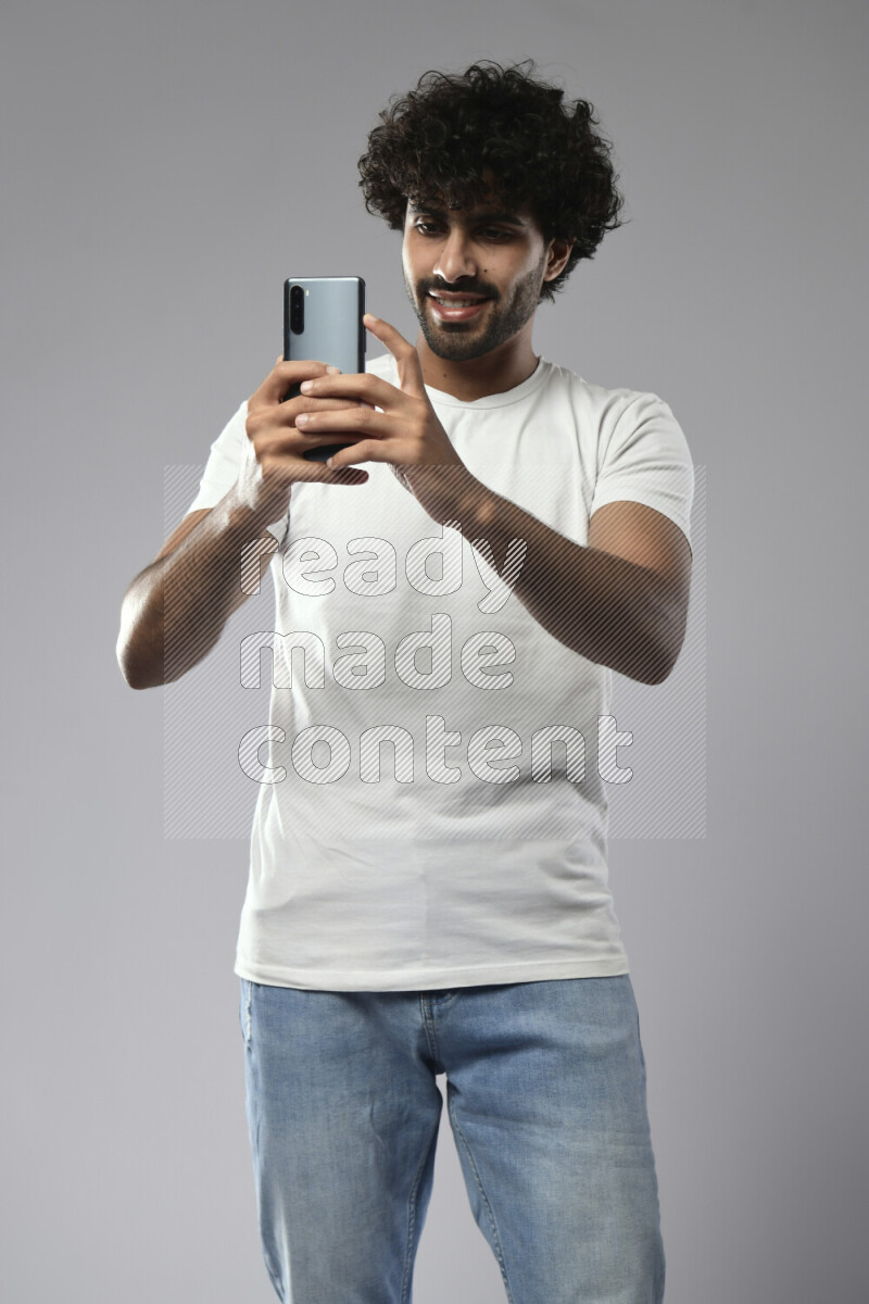 A man wearing casual standing and shooting with his phone on white background