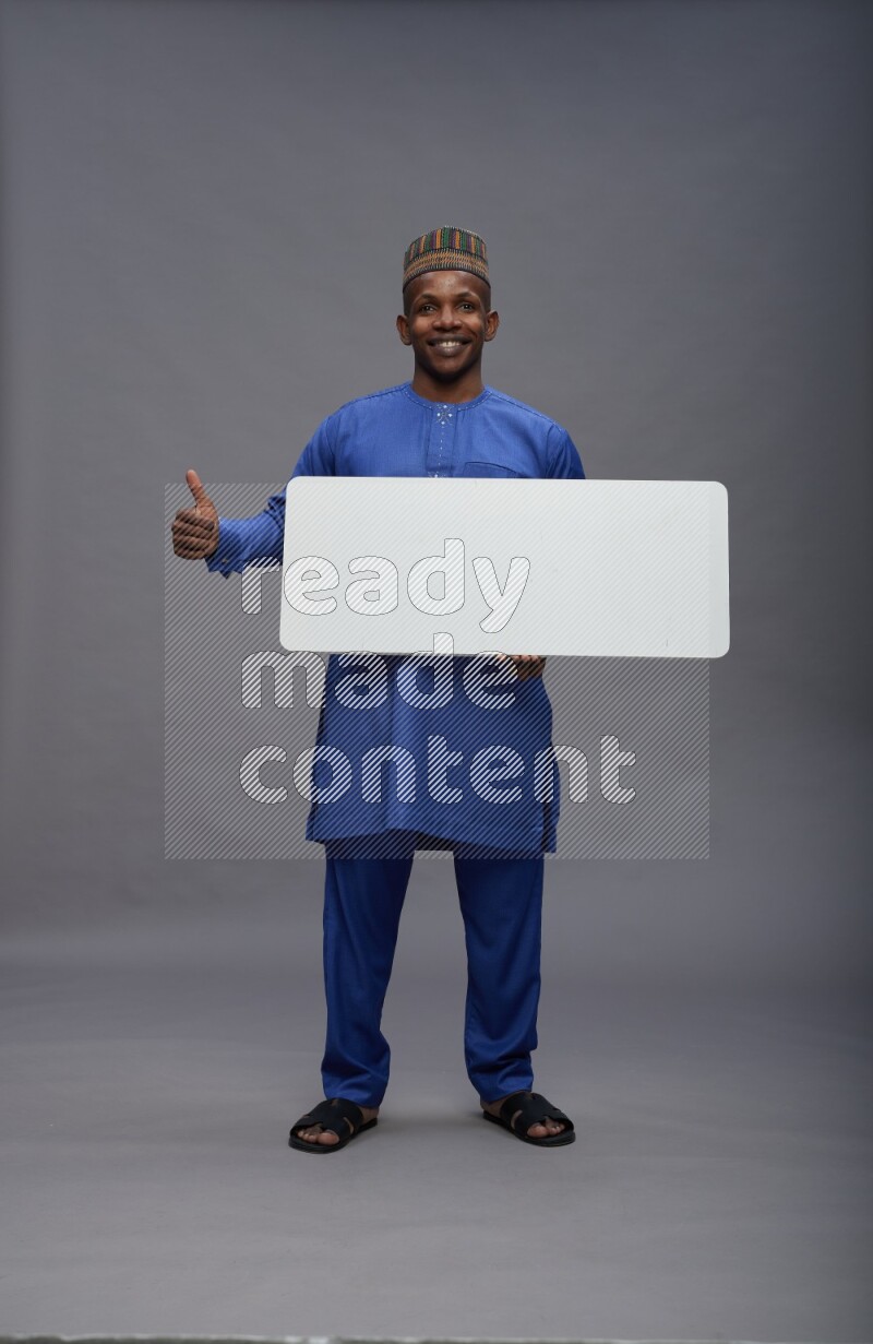 Man wearing Nigerian outfit standing holding board on gray background