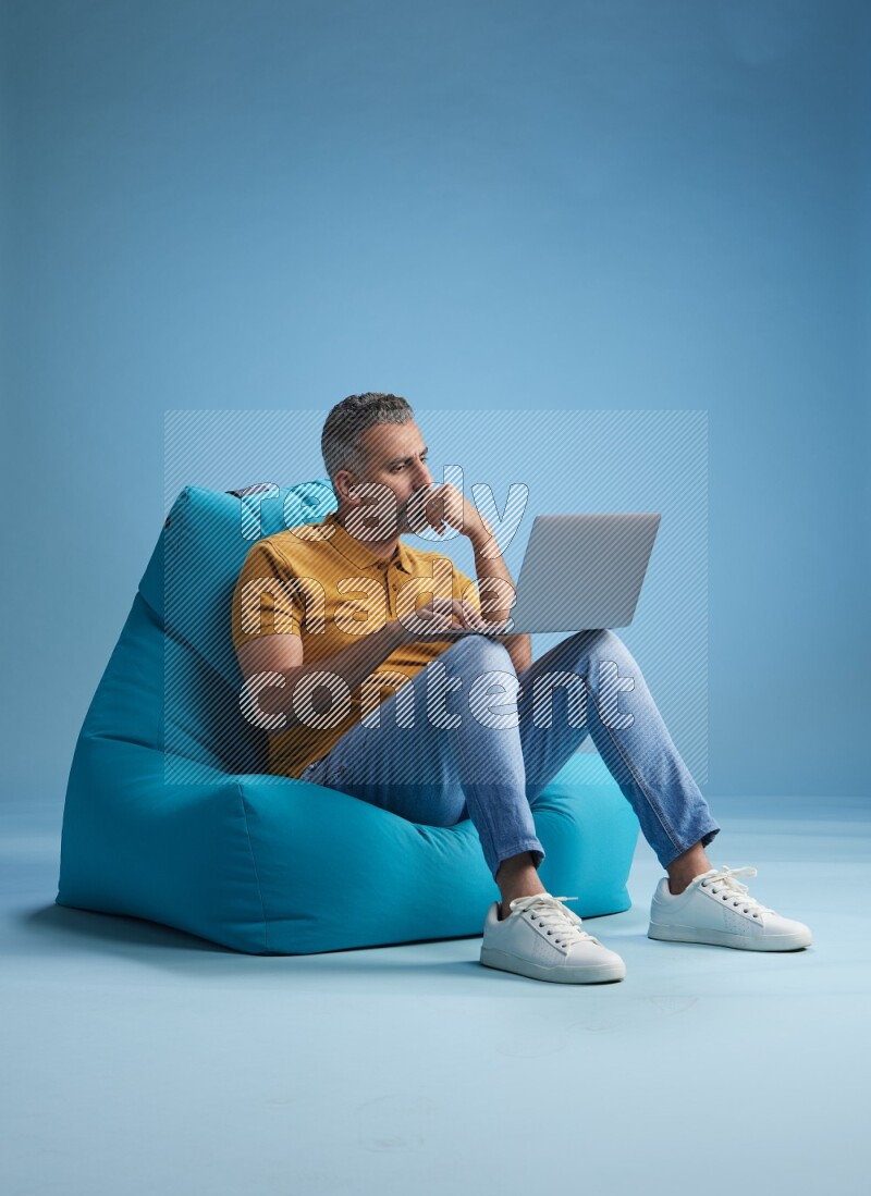 A man sitting on a blue beanbag and working on laptop