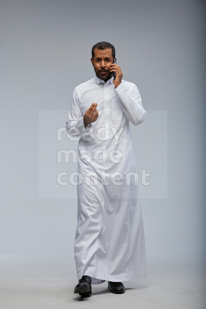 Saudi man wearing Thob standing talking on phone on Gray background