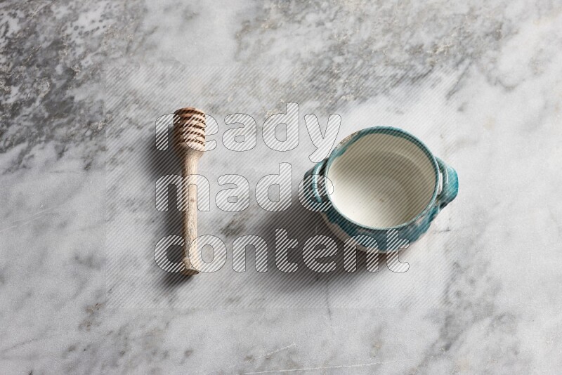 Multicolored pottery bowl with wooden honey dipper on the side on grey marble background
