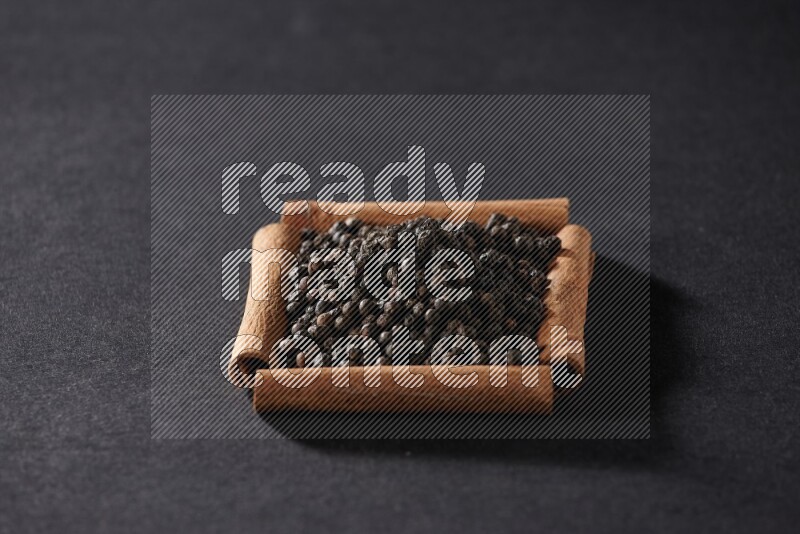 A single square of cinnamon sticks full of black pepper on black flooring