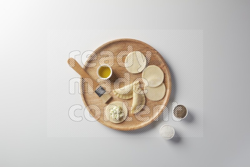 two closed sambosas and one open sambosa filled with cheese while salt, black pepper and oil with oil brush aside in a wooden dish on a white background