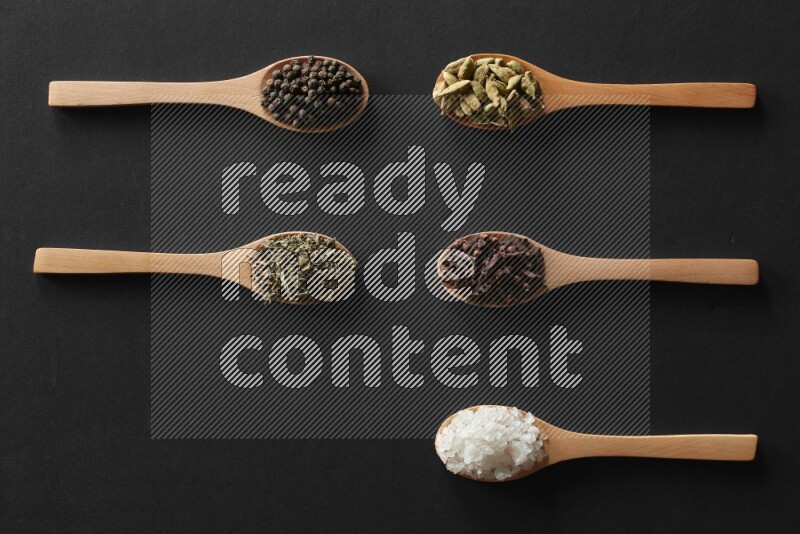 الفلفل الأبيض والقرنفل والهيل والملح والفلفل الأسود وريحان مجفف في معالق خشبية علي خلفية سوداء