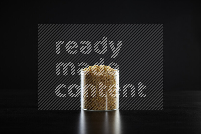 Coarse bulgur in a glass jar on black background