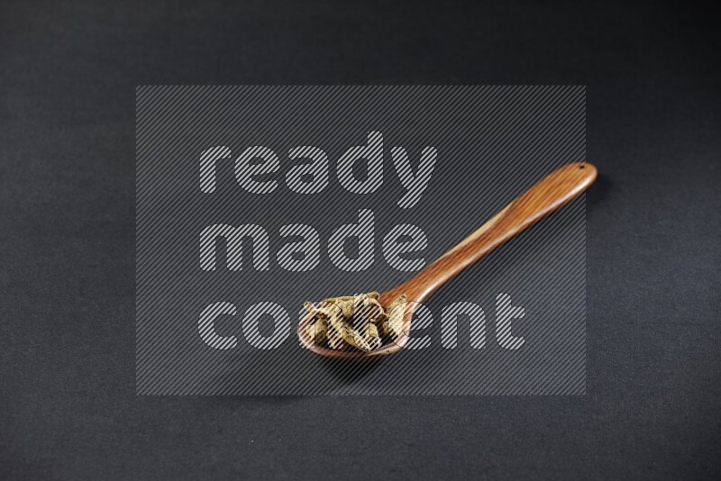 A wooden ladle full of dried turmeric fingers on black flooring