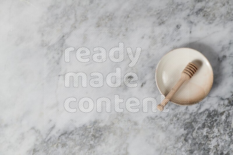 Beige pottery plate with wooden honey dipper in it on grey marble background
