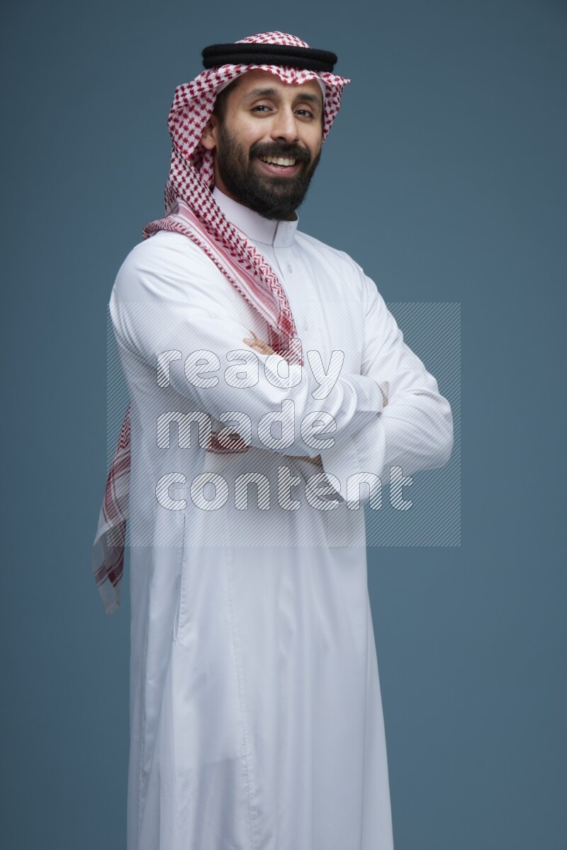 A man posing in a blue background wearing Saudi Thob and Shomag
