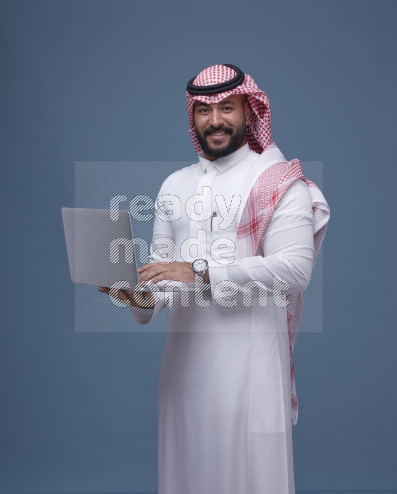 A Saudi man Holding a Laptop on Blue Background wearing Saudi Thob and Shomag