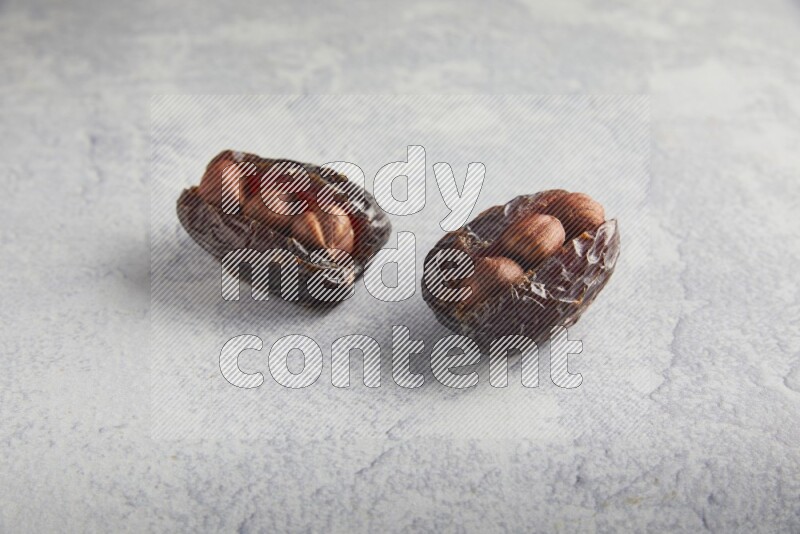 two hazelnuts stuffed madjoul dates on a light grey background