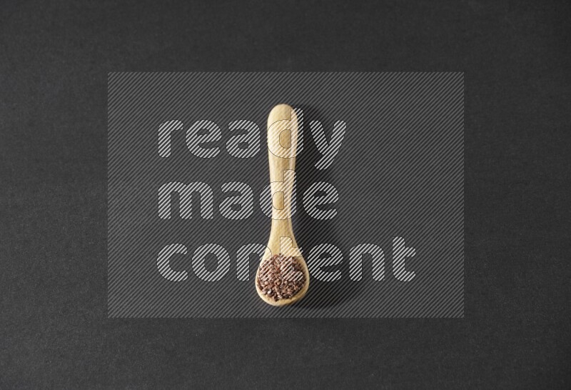 A wooden spoon full of flaxseeds on a black flooring