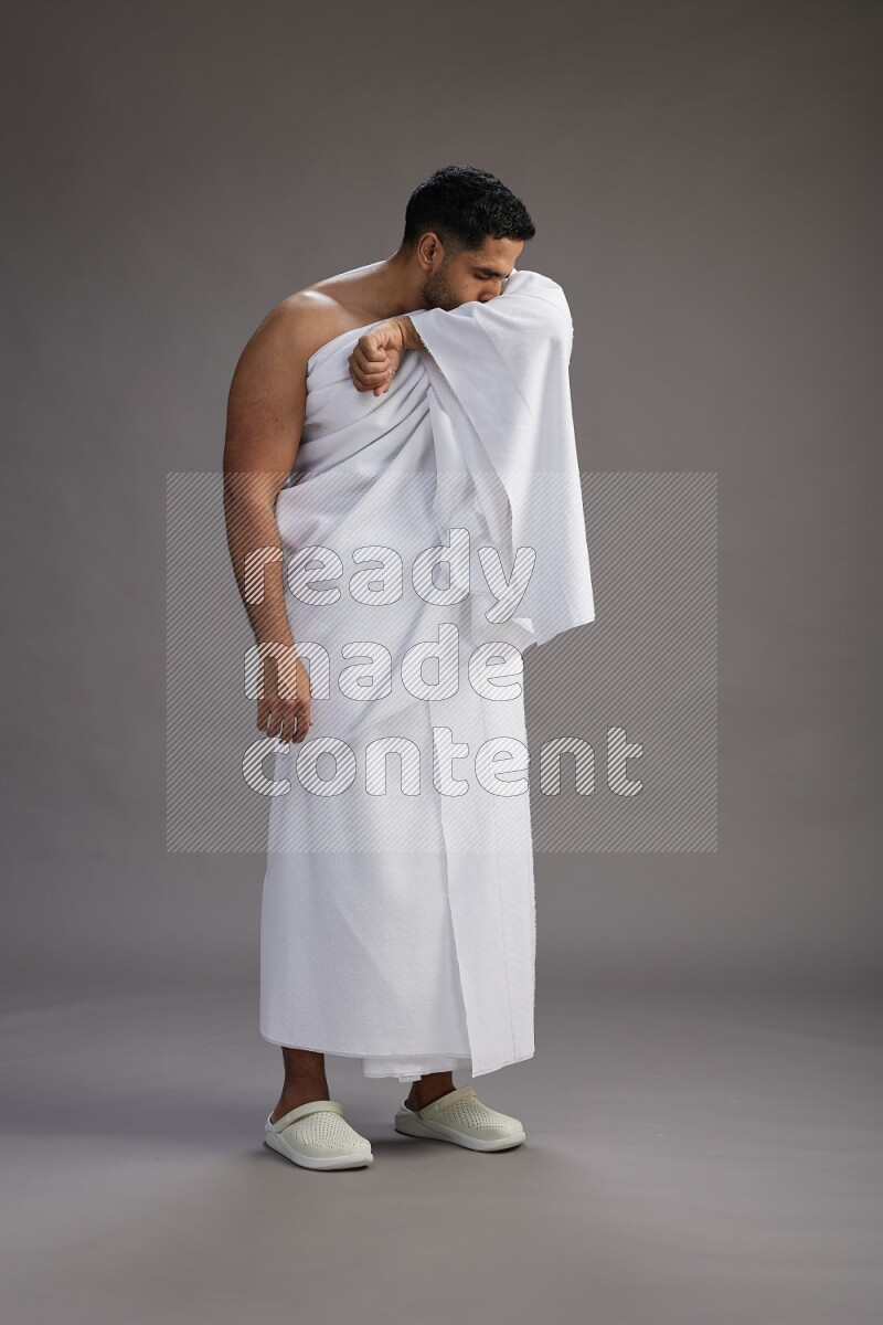 A man wearing Ehram standing showing how to sneeze on gray background