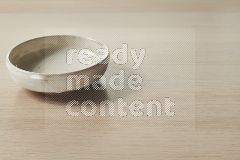 A beige pottery bowl on light wooden background