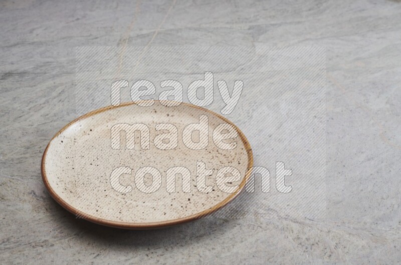 A beige pottery plate on grey marble background