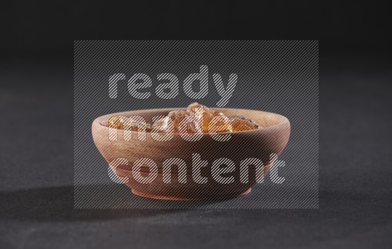A wooden bowl full of gum arabic on a black flooring