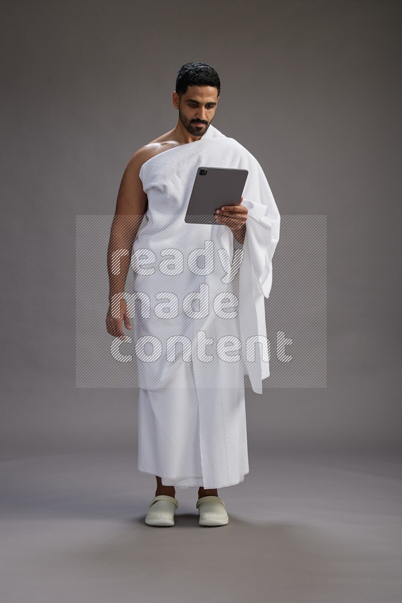 A man wearing Ehram and holding a tablet on gray background