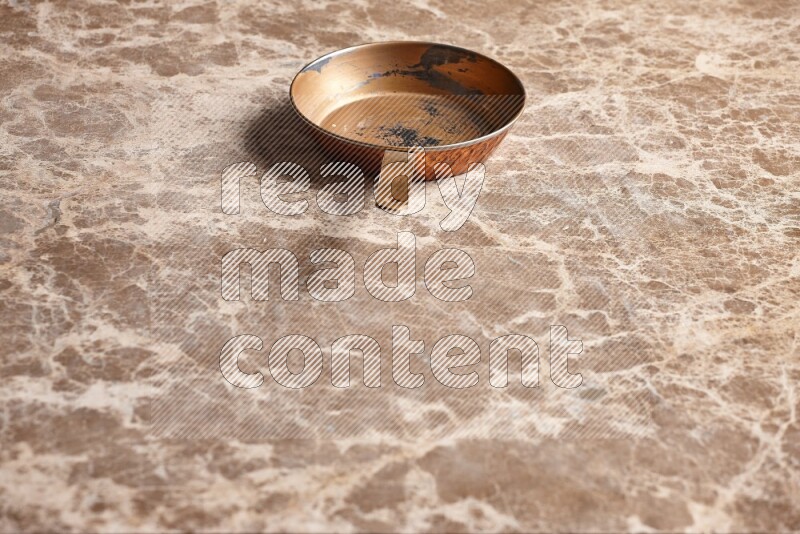 A small copper pan on beige marble background