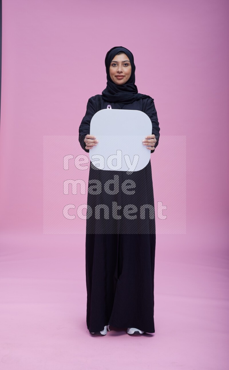 Saudi woman wearing pink ribbon on Abaya standing holding social media signs on pink background