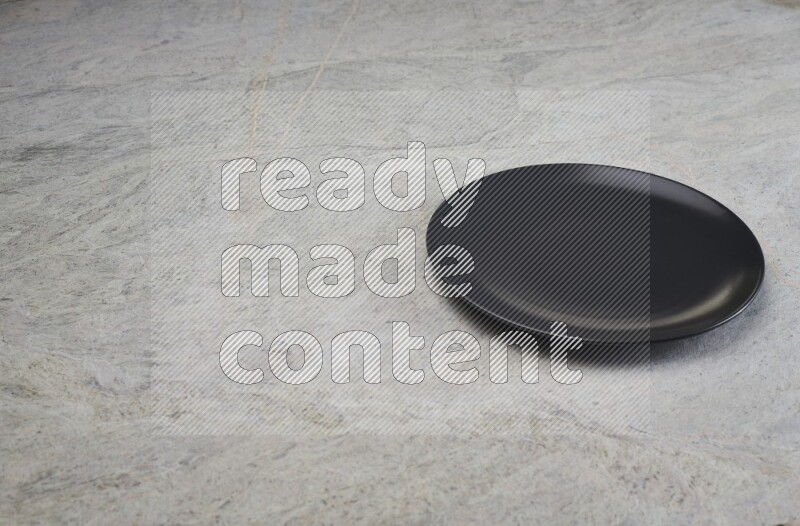 A black ceramic circular plate on grey marble background