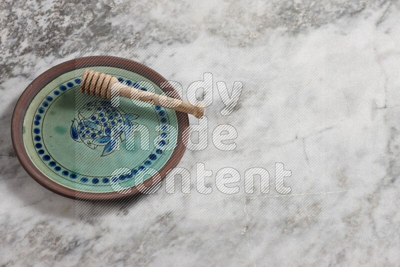 Decorative pottery plate with wooden honey dipper in it on grey marble background
