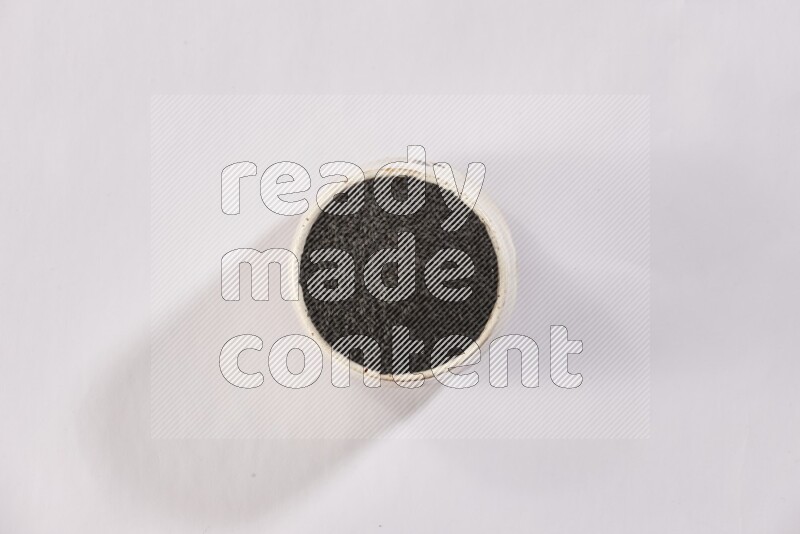 A beige pottery bowl full of black seeds on white flooring