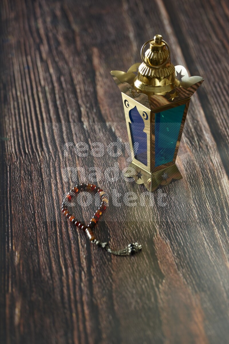 A golden lantern with different drinks, dates, nuts, prayer beads and quran on brown wooden background
