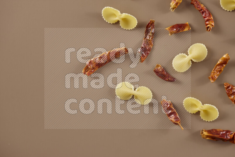 Raw pasta with different ingredients such as cherry tomatoes, garlic, onions, red chilis, black pepper, white pepper, bay laurel leaves, rosemary and cardamom on beige background