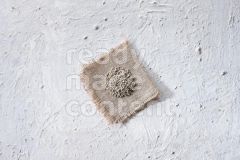 White pepper beads on a burlap piece of fabric on textured white flooring