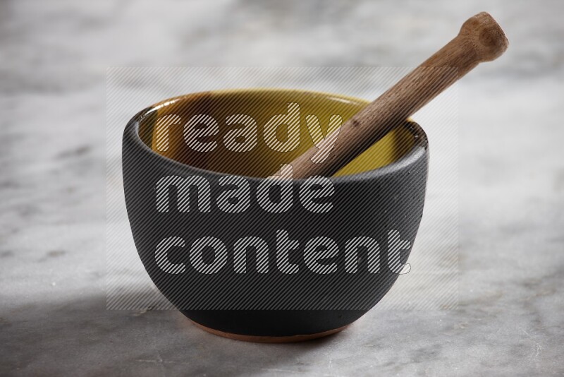 Multicolored pottery bowl with wooden honey dipper in it on grey marble background