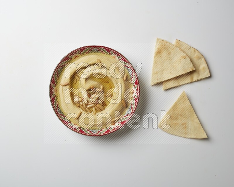 Hummus in a red plate with patterns garnished with pine nuts on a white background