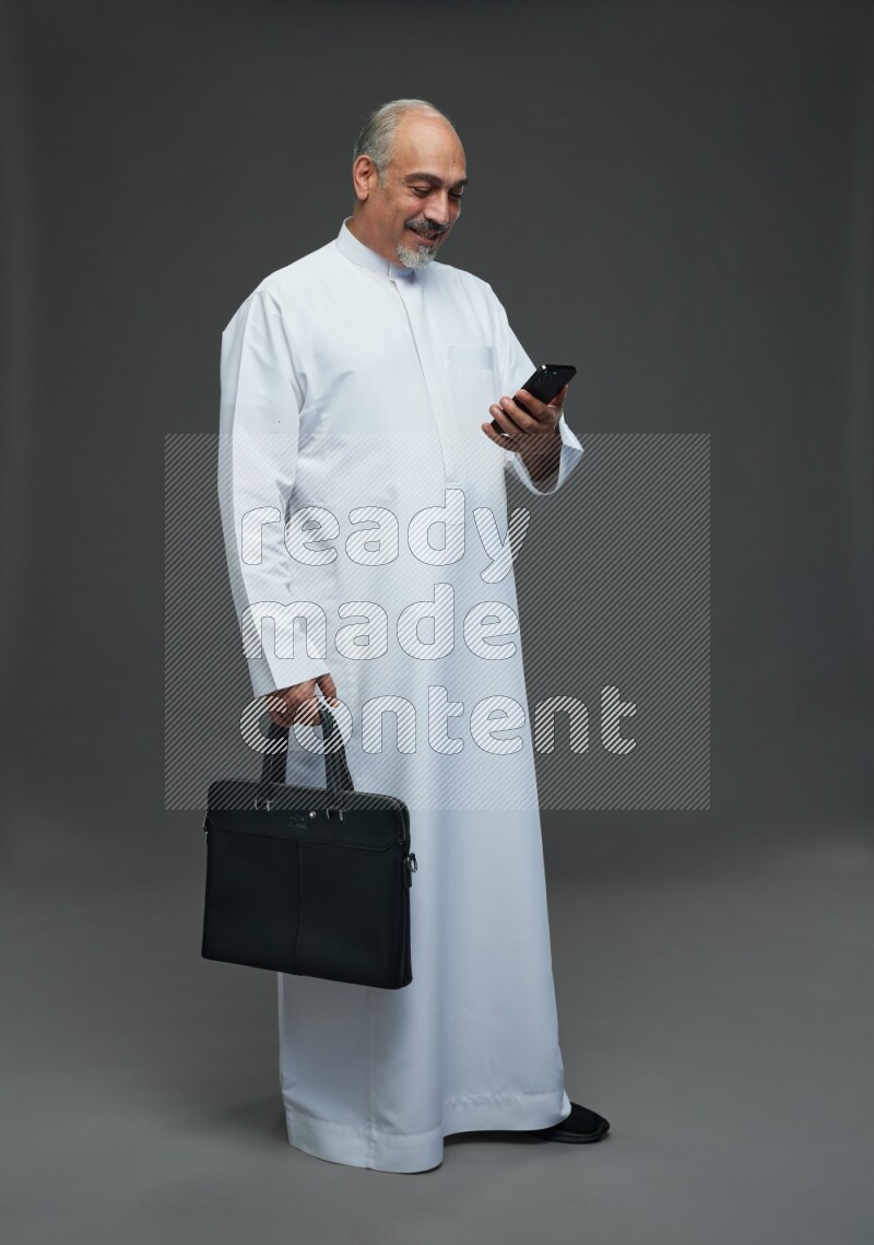 Saudi man without shomag Standing holding bag and phone on gray background