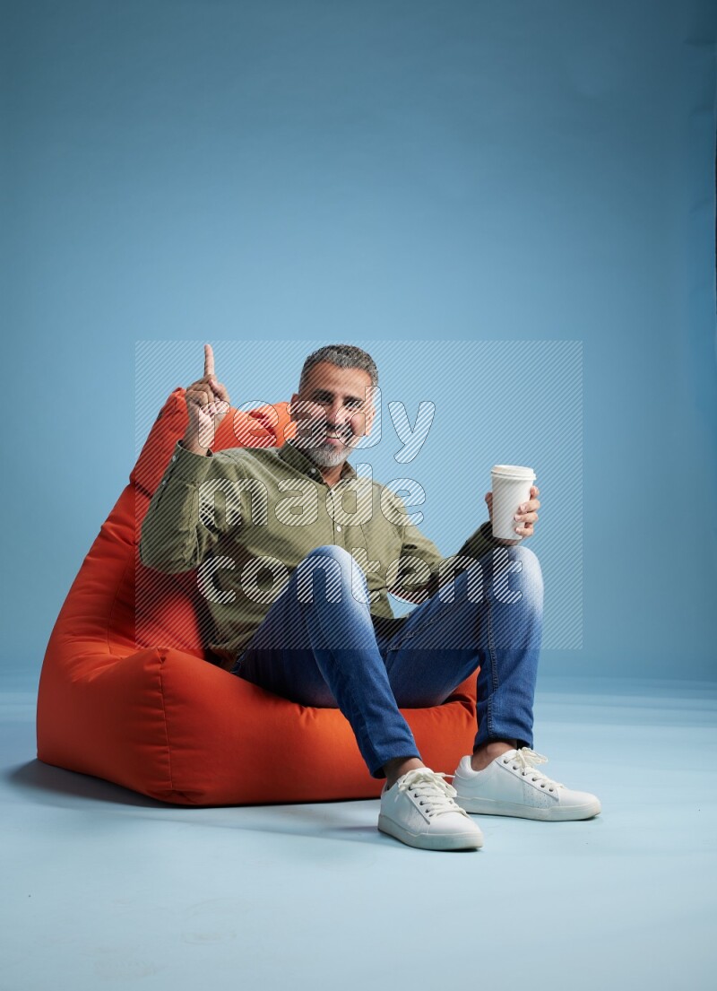A man sitting on an orange beanbag and drinking coffee