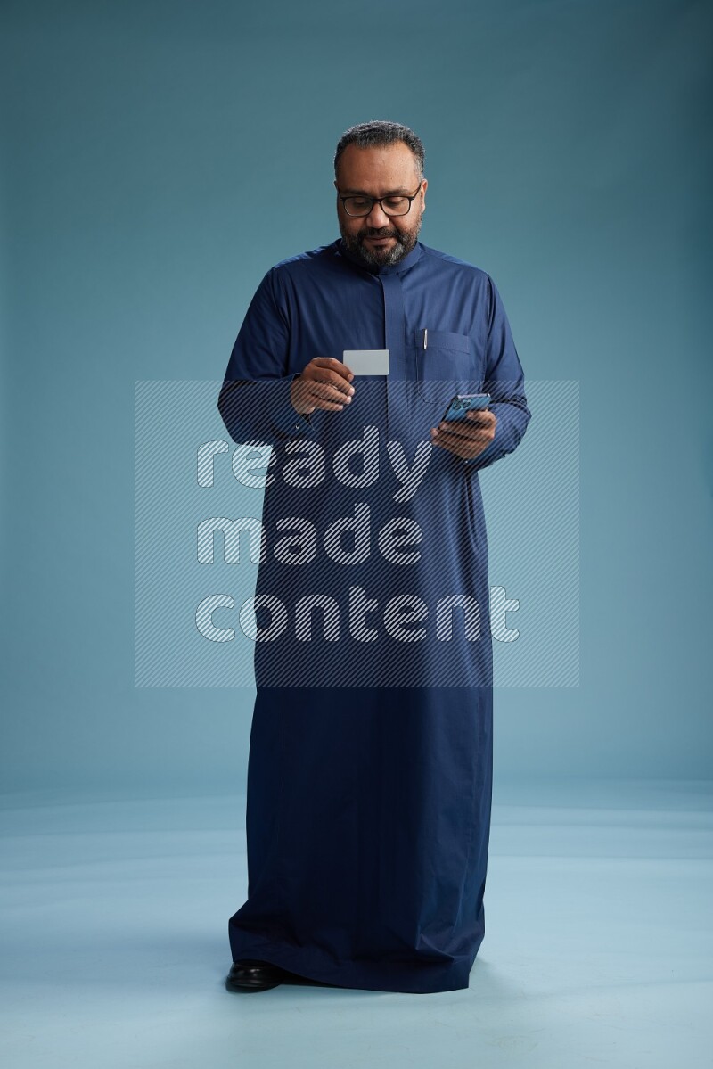 Saudi Man without shimag Standing holding ATM while talking on phone on blue background