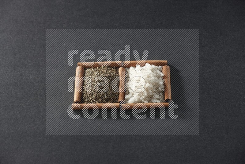 مربعان من أعواد القرفة ممتلئان بالملح الأبيض وحبوب الكمون علي خلفية سوداء