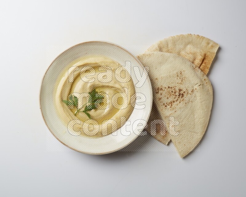 Hummus in a pottry plate garnished with parsley on a white back ground