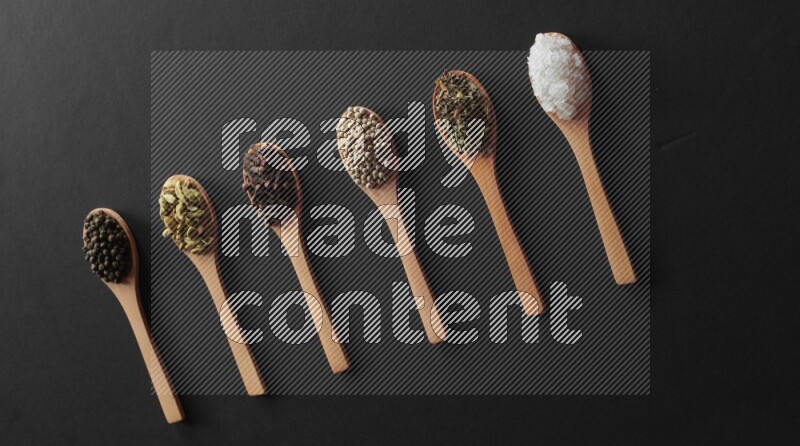 الفلفل الأبيض والقرنفل والهيل والملح والفلفل الأسود وريحان مجفف في معالق خشبية علي خلفية سوداء