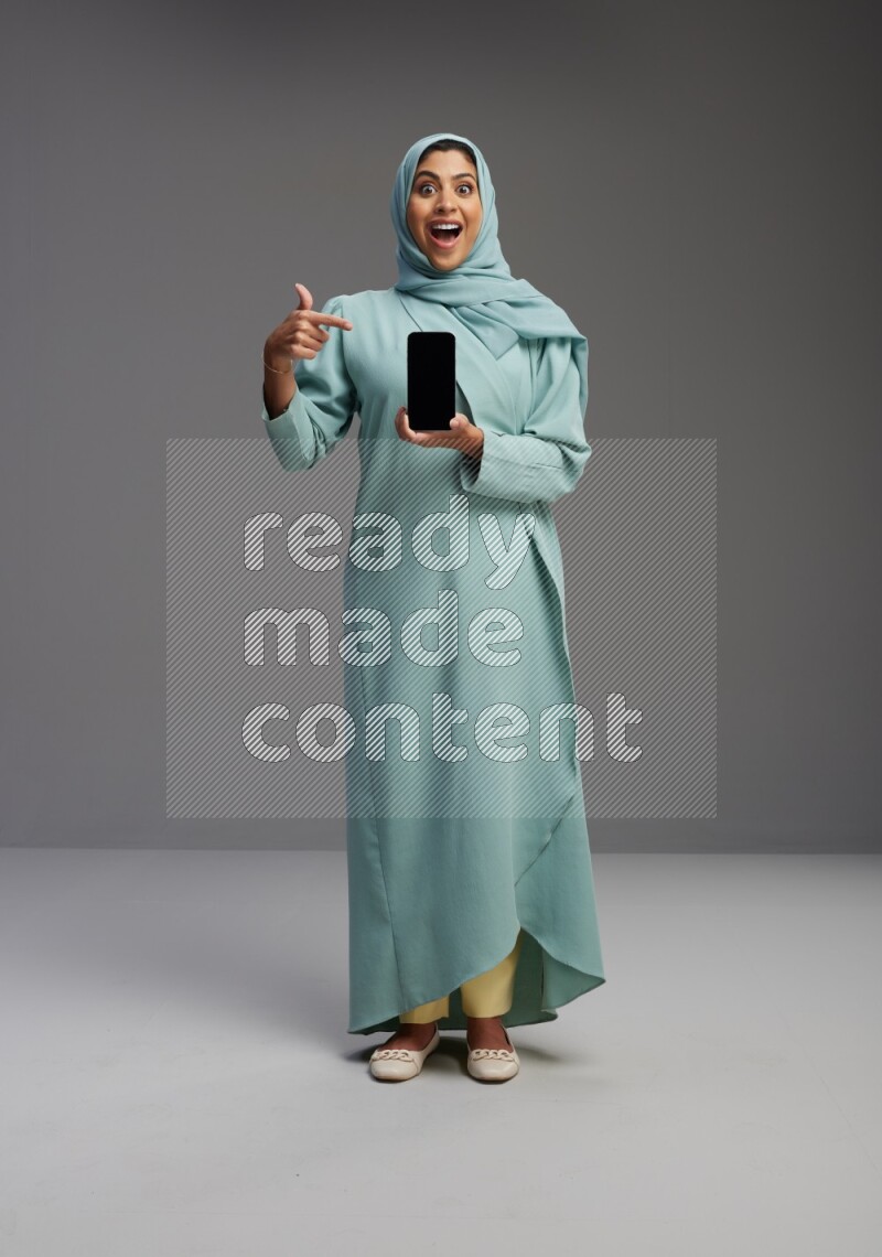 Saudi Woman wearing Abaya standing showing phone to camera on Gray background